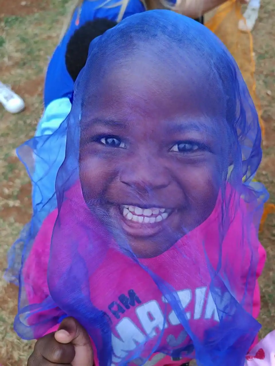 A child at Lusana smiling through a coloured scarf