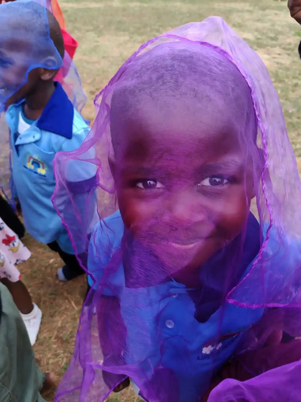 Child peeking through a purple scarf at Lusana