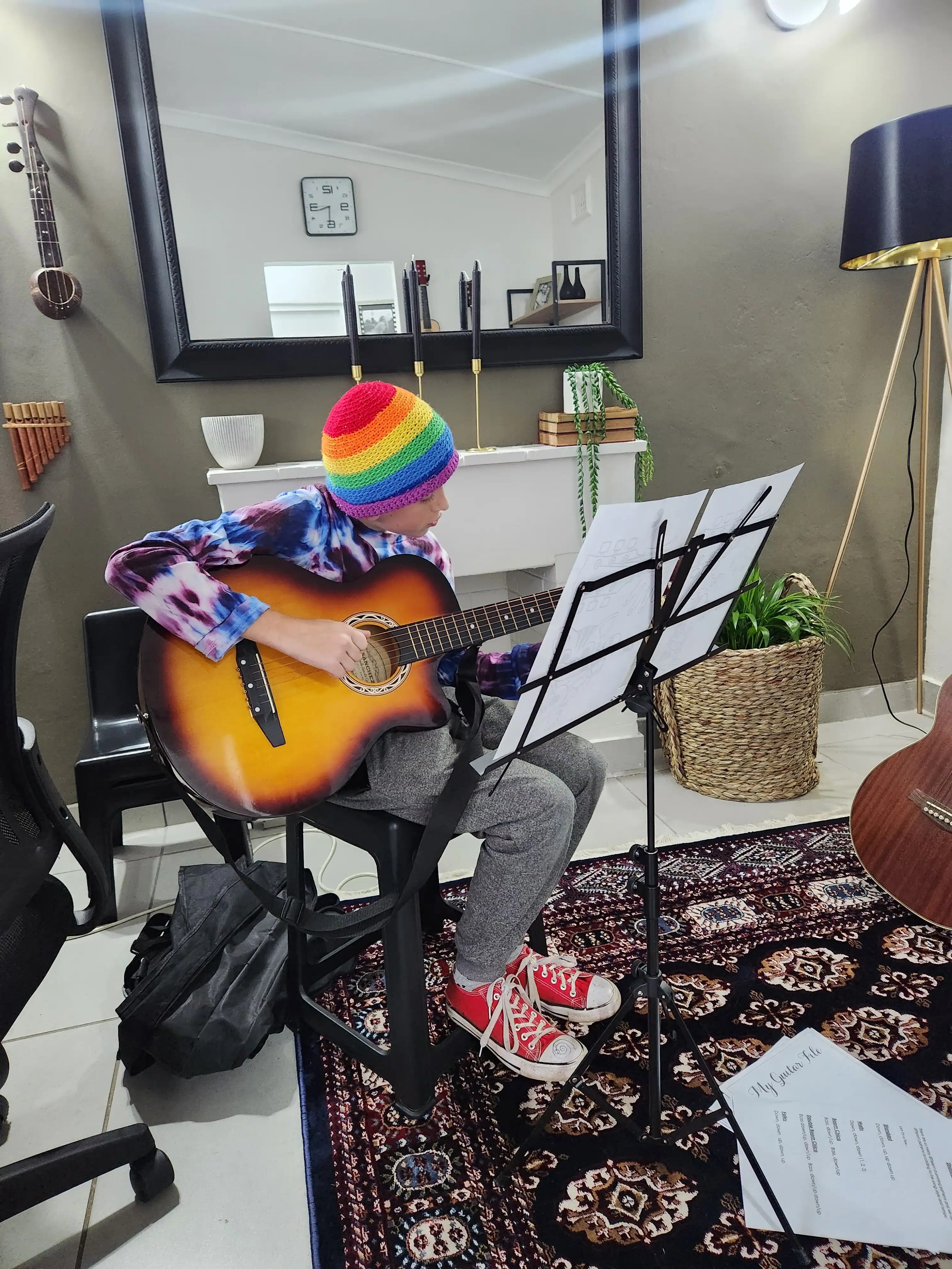 Child in rainbow beanie playing guitar at Little Musos private lesson